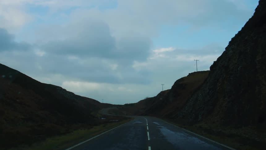 Wet highway surrounded by mountains on a cloudy day