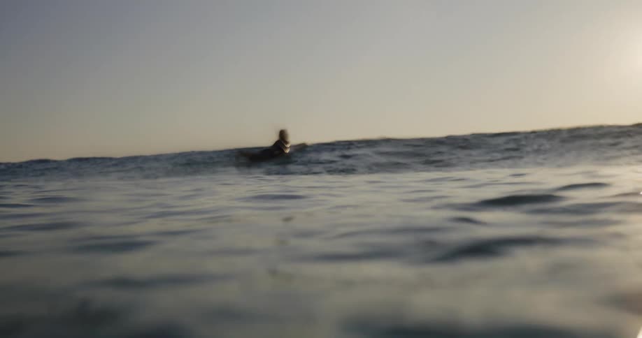 Surfer isolated in an ocean with the sun on the horizon