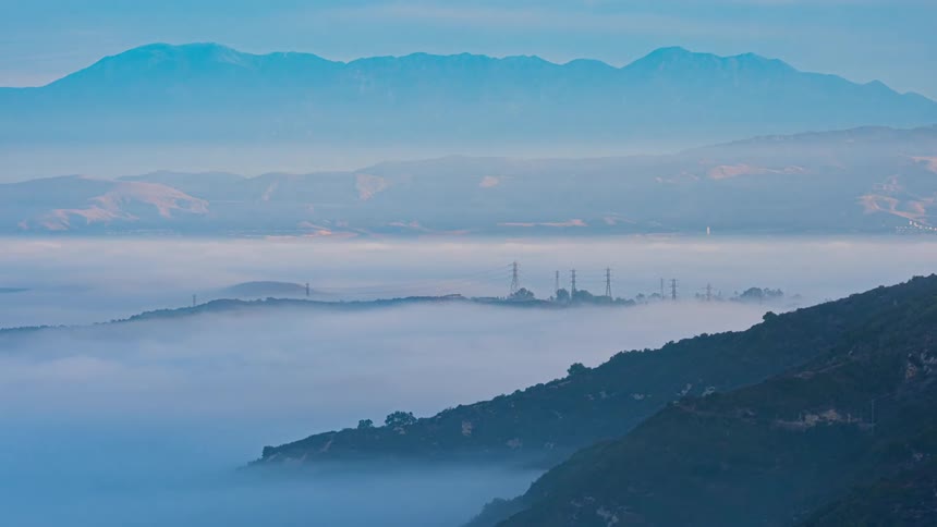 Dense fog obscures coastal mountains during the daytime