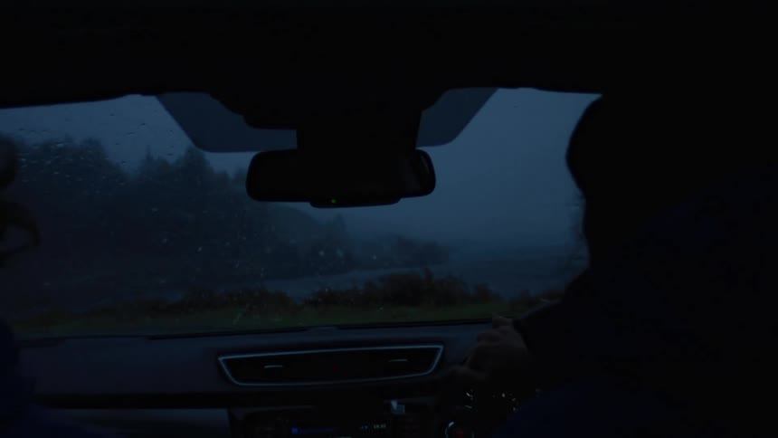 Interior view of silhouette of two people sitting in the front seat of a moving vehicle with the windshield up