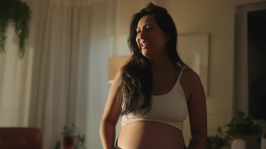 Pregnant woman showing her belly in front of a smartphone on a tripod in the living room