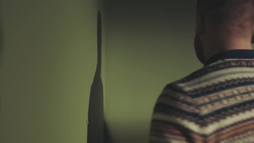 Man in a striped sweater measuring corner walls with a measuring tape