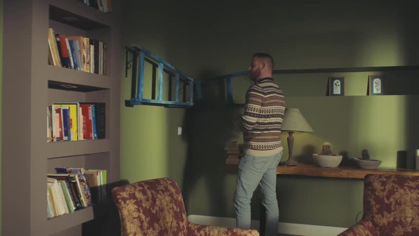 Man fitting a laddershaped bookshelf into the corner of a wall and placing a book next to it