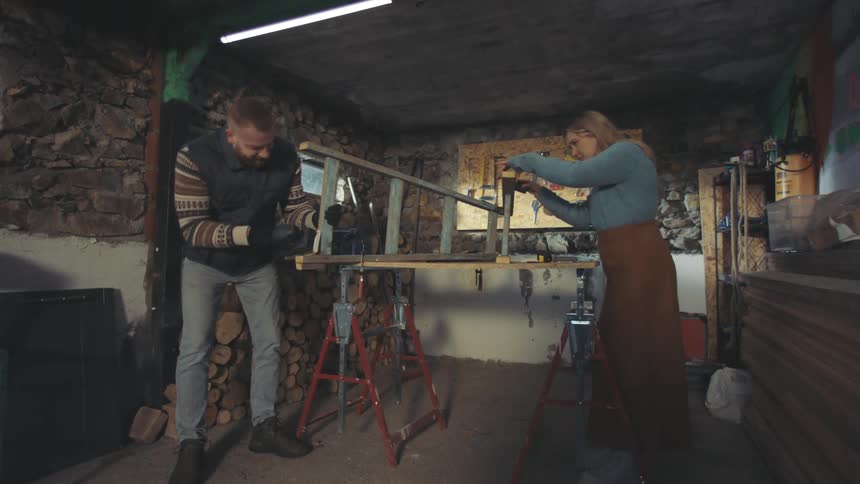 Woman and a man in a workshop working together on a wooden ladder on the table