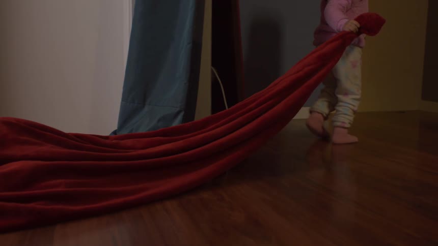 Child dragging a red velvet blanket across hardwood floor