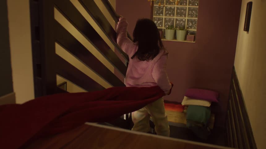 A child slowly walks down the stairs dragging a blanket