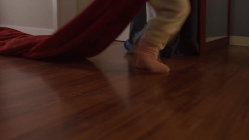 Child walks across a wooden floor in socks while dragging a blanket