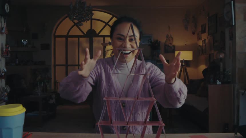 Woman getting happy as she finishes a stack of cards balanced on top of a table
