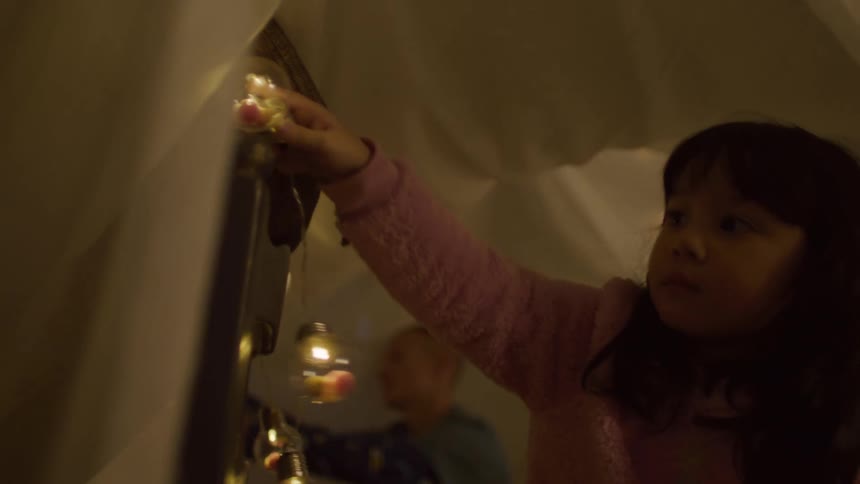 A little girl placing some shiny decorative balls on the back of a chair that has a sheet on top
