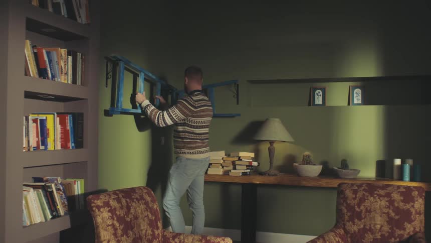 A man places a ladder on the wall hooks