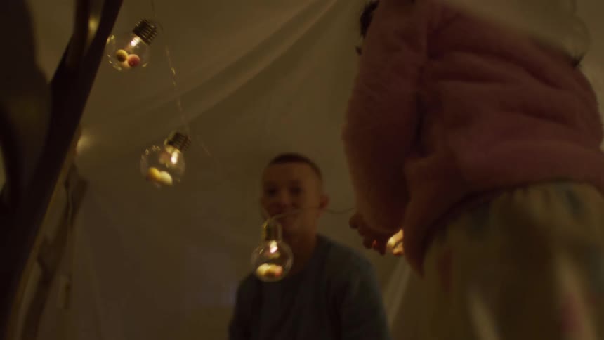 Children are arranging christmas lights on a makeshift fort made of blankets