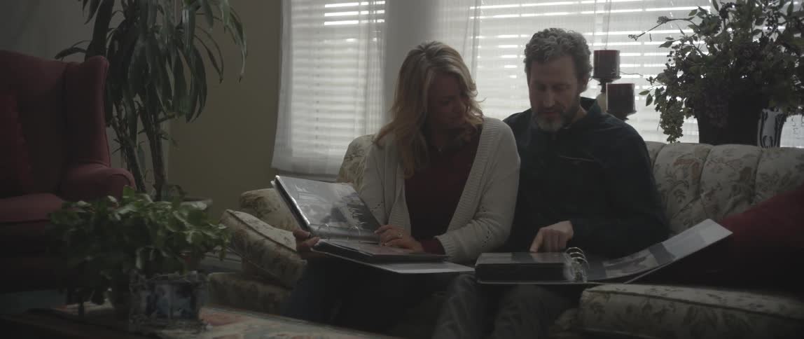 A man and woman look at photo albums on a couch