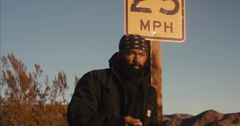Man holding a rock while leaning against a highway sign in a desert location