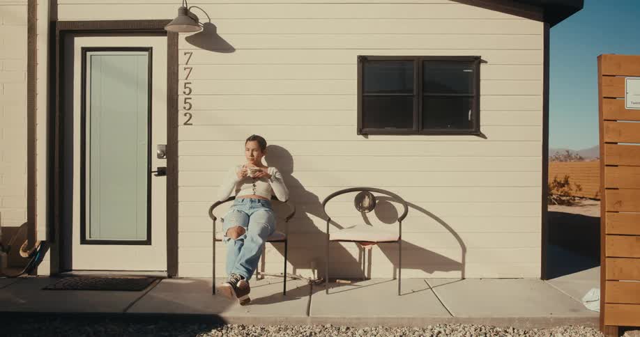 Woman leaving her house and sitting on a chair in the backyard drinking coffee