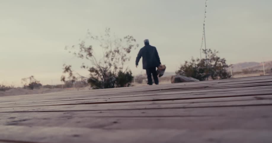 Man picking up a piece of firewood and carrying it across an open landscape