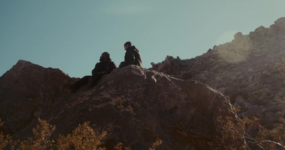 Two people sitting on a rock talking in a valley
