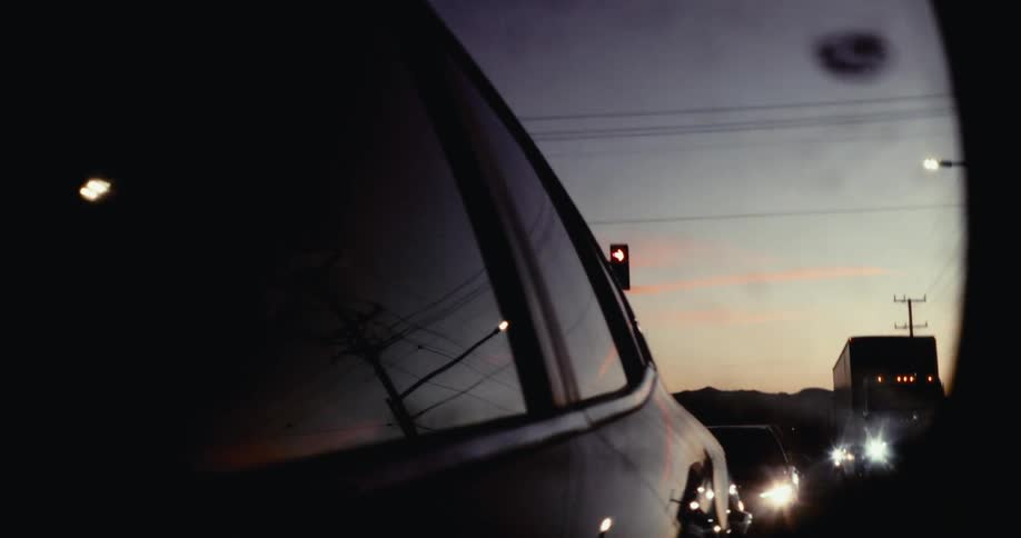 A cars side mirror reflects a blurry dusky scene with faint lights seen from inside the vehicle through the partially open window