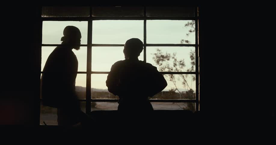 Silhouette of a woman opening a window curtain and a man standing outside the house