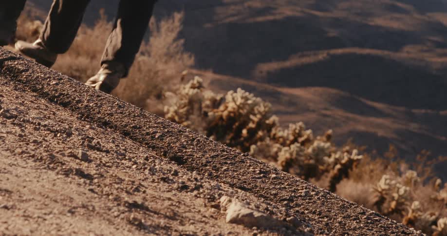 Legs of two people walking on a paved street with mountains in the background