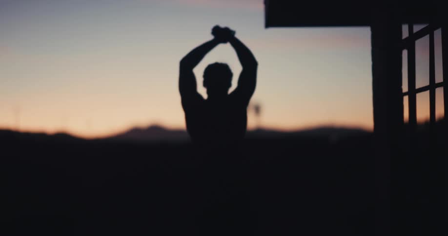 The silhouette of a person stretching their arms upwards in a very dark morning environment