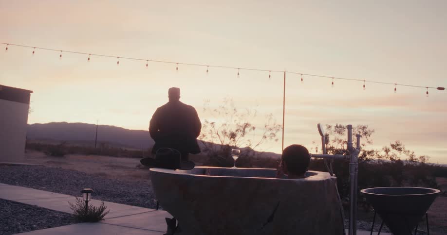 Man walking outdoors next to a bathtub with a woman