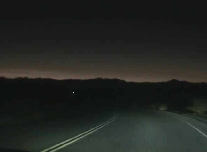 Dark and deserted road with double yellow lanes follows a curve and mountains in the background under a dark sky