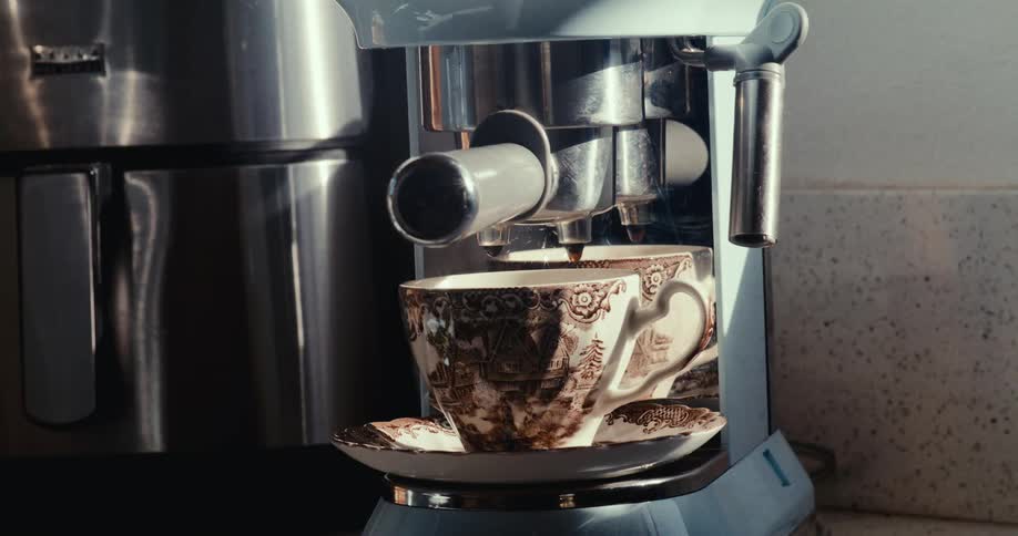 A persons hand placing a white mug with brown details into a coffee machine and then waiting for the coffee to pour the liquid inside