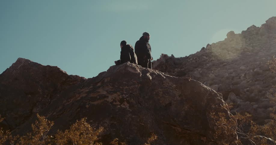 Two people are standing on a rock in a desert region on a clear sky day