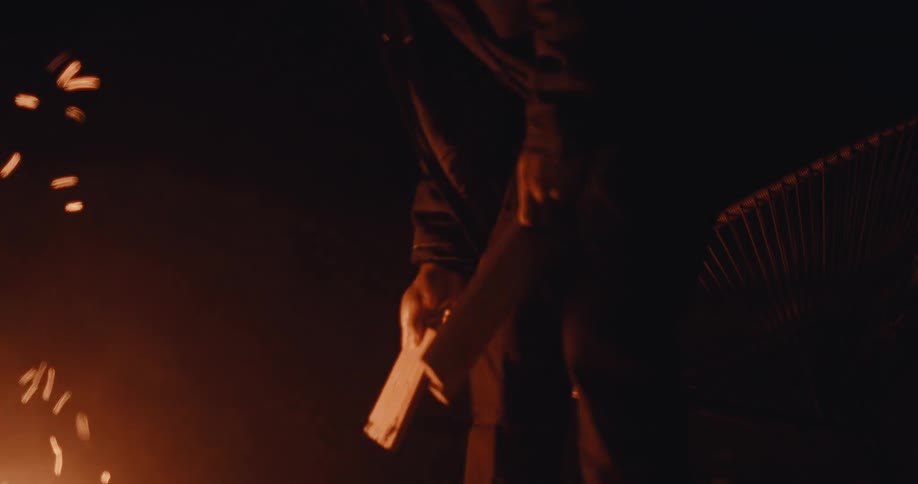 Man throwing small pieces of firewood into a campfire at night