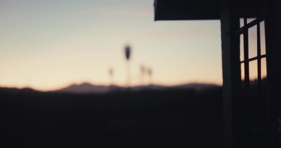 A silhouette of a building with a window is set against a sunset backdrop with mountains in the distance