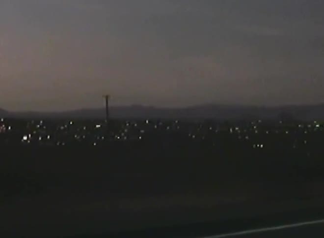 Moving view of a highway at dusk with city lights and mountains in the background