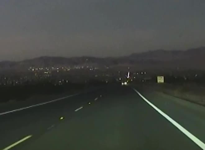 Highway with vehicle traffic at night with a city and mountains in the background