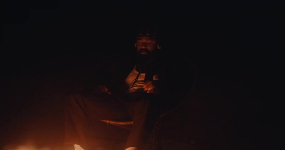 A man is sitting in front of a fire in a dark outdoor environment