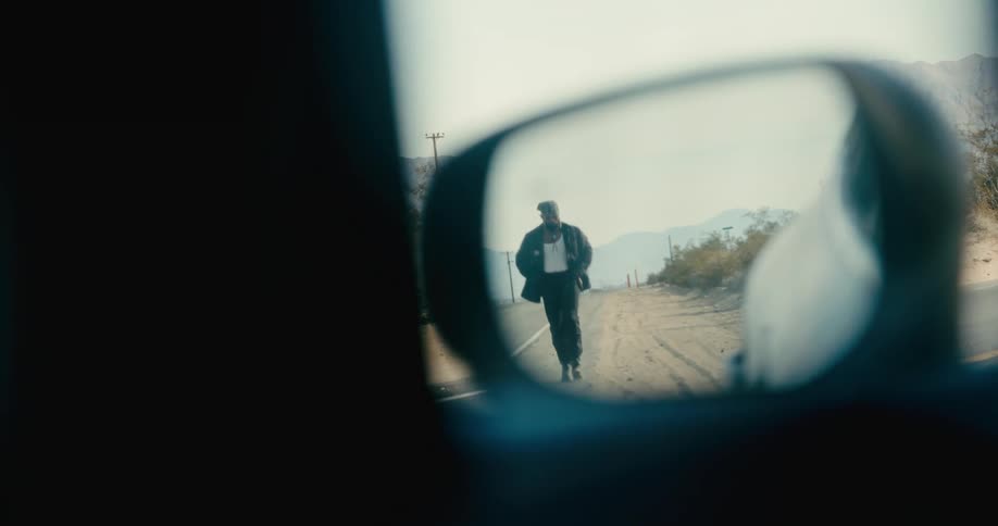 A man walks down a desert road as seen in a cars side mirror