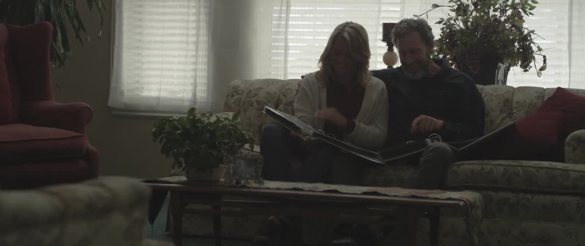 A man and woman look at photo albums while sitting on a couch