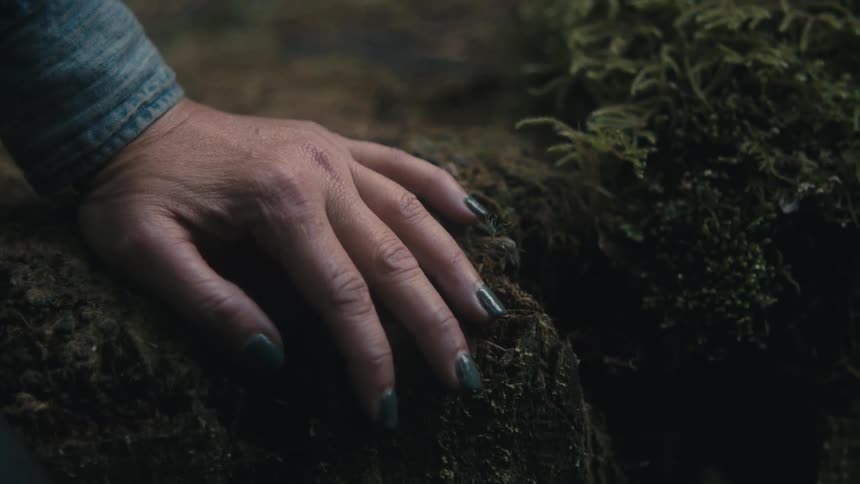 Woman with painted fingernails sits outdoors on a moss covered surface