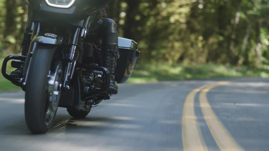 Motorcyclist rides a motorcycle along a highway passing through the woods on a summer day