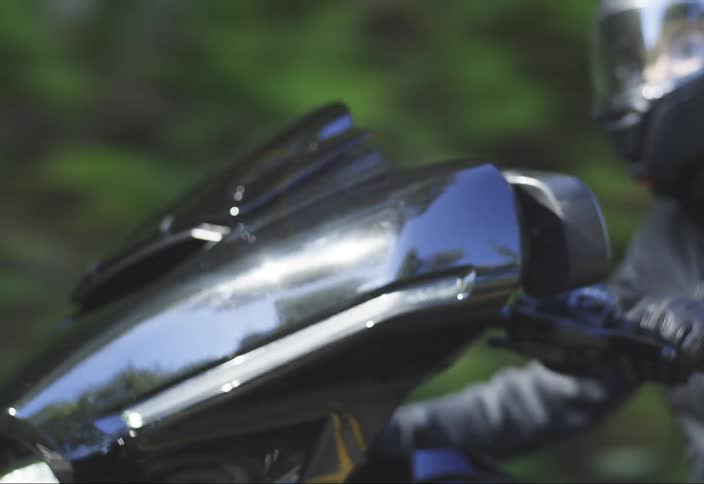 Motorcyclist in a black jacket and leather gloves rides a black motorcycle while wearing a helmet with a closed visor