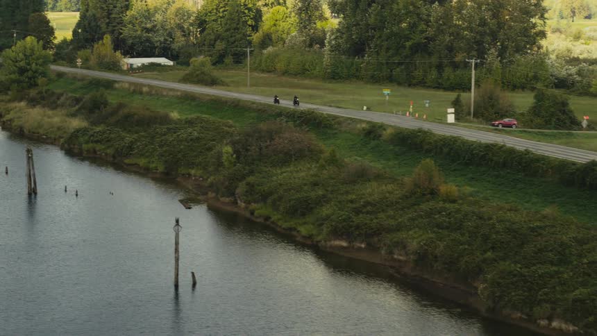 Two motorcycles traveling along a paved road by a lake