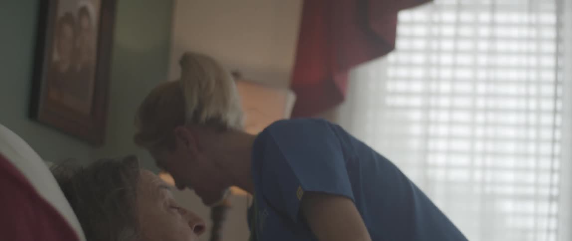 A nurse gives an elderly woman a sip of water and sits down