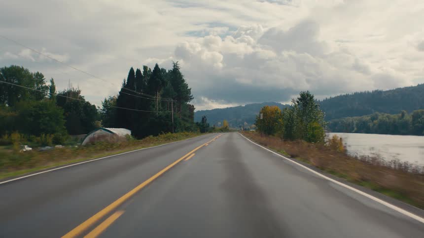 An asphalt road in a rural area where there is a huge lake on the left side surrounded by trees