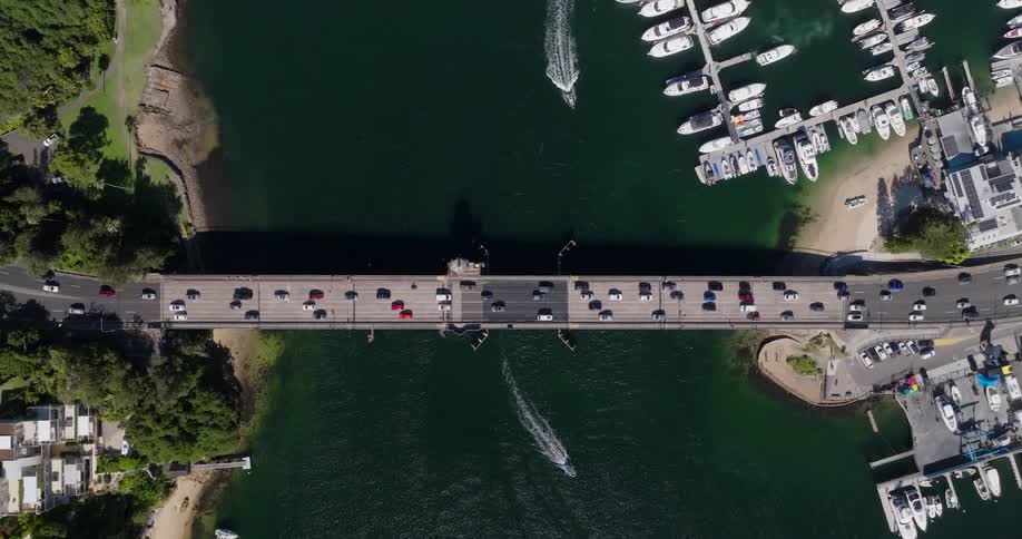 Boats leave a wake while moving near the busy bridge connecting a residential neighborhood to the marina