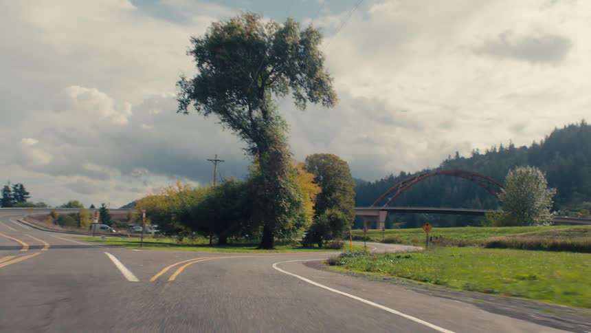 A forked road through a wooded area with an arched red bridge in the background under a partly cloudy sky