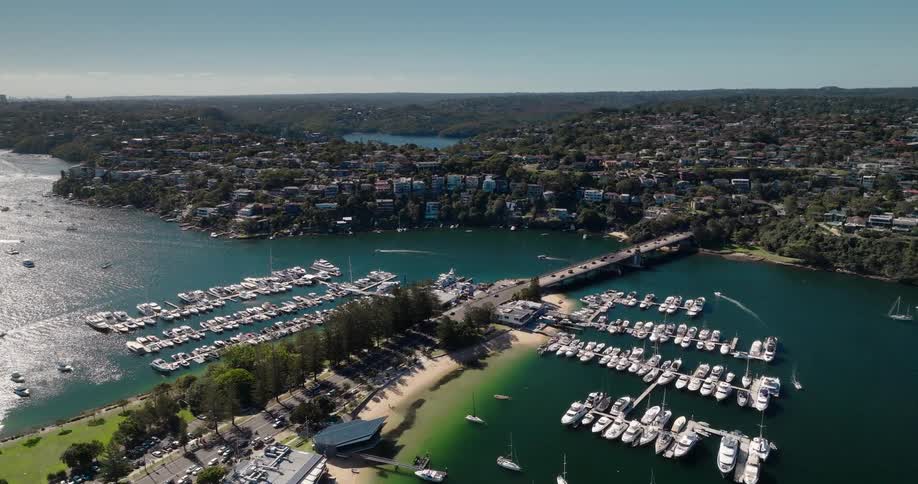 Aerial view shows a marina with several anchored boats surrounded by beaches green areas and a city with houses and buildings spread among hills