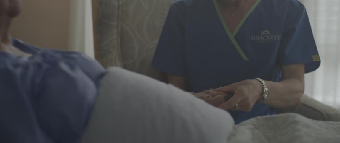 A woman sitting bedside rubs the woman's hand lying down