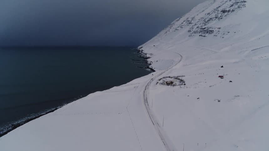 Aerial view of a road with vehicle traffic on a snowy mountain by the sea on a cloudy day