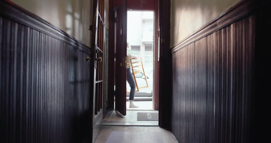 Woman carrying a chair down a hallway opening the door and walking out
