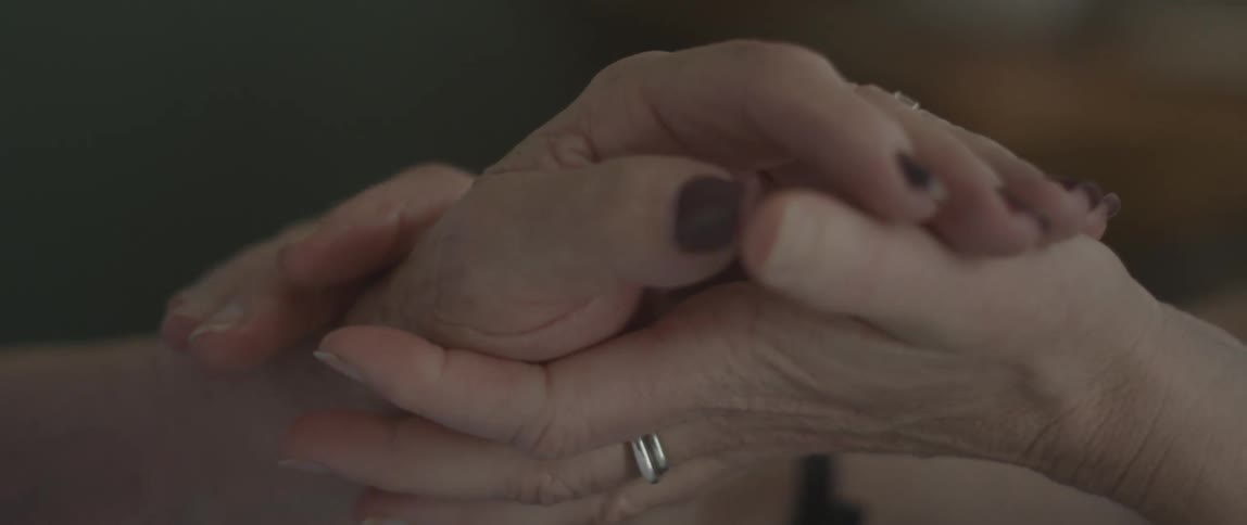 A woman rubs and clasps the hand of an elderly woman
