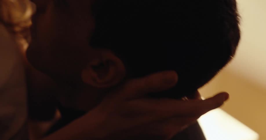 A young couple cuddles closely while talking in a cozy dimly lit room at home