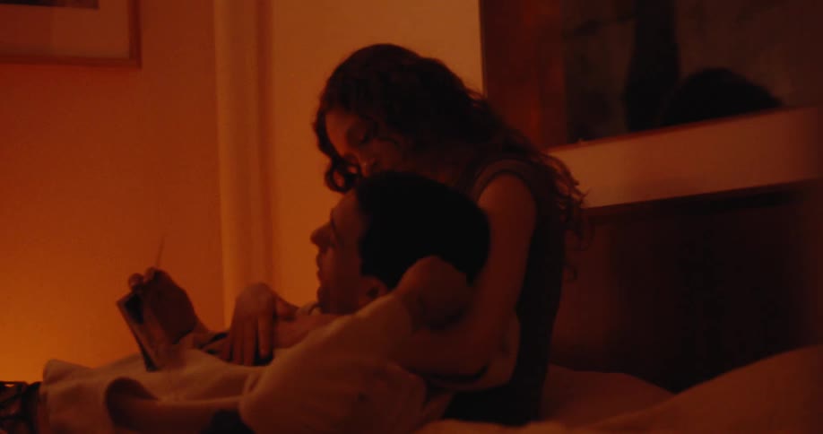 A woman and a man are lying on a bed and the woman is hugging the mans head and the room has a red light